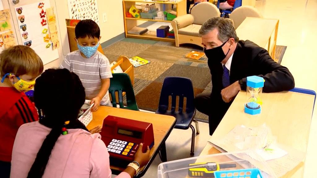 Governor Roy Cooper stops to speak to children and an educator playing with supermarket type toys