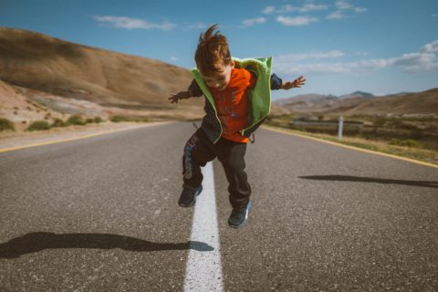 young boy jumping in empty road with mountains behind him