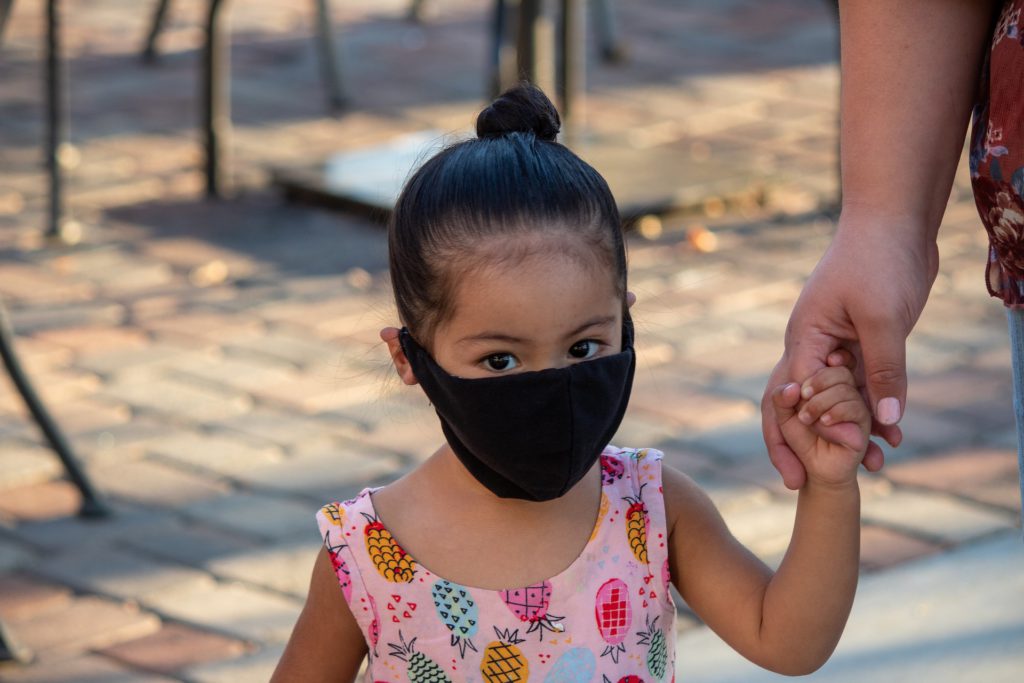 Young girl wearing mask holding hand of adult