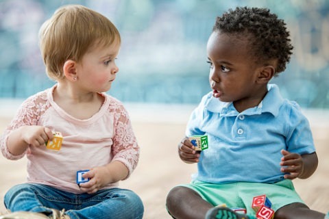 2 young toddlers playing with blocks looking at each other