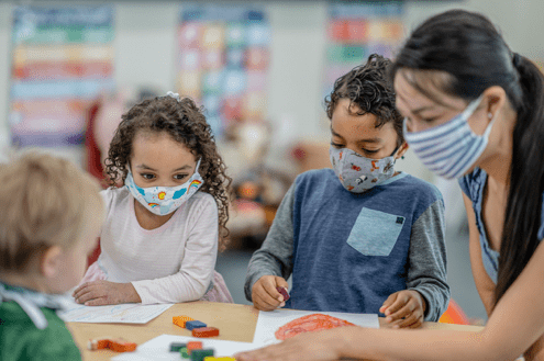 young kids and teacher wearing masks in classroom