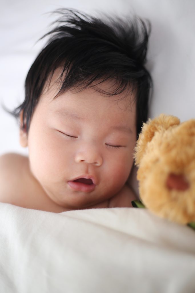 A baby sleeping next to a stuffed bear