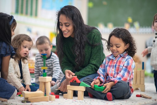 Teacher plays with blocks on floor with 4-5 young children
